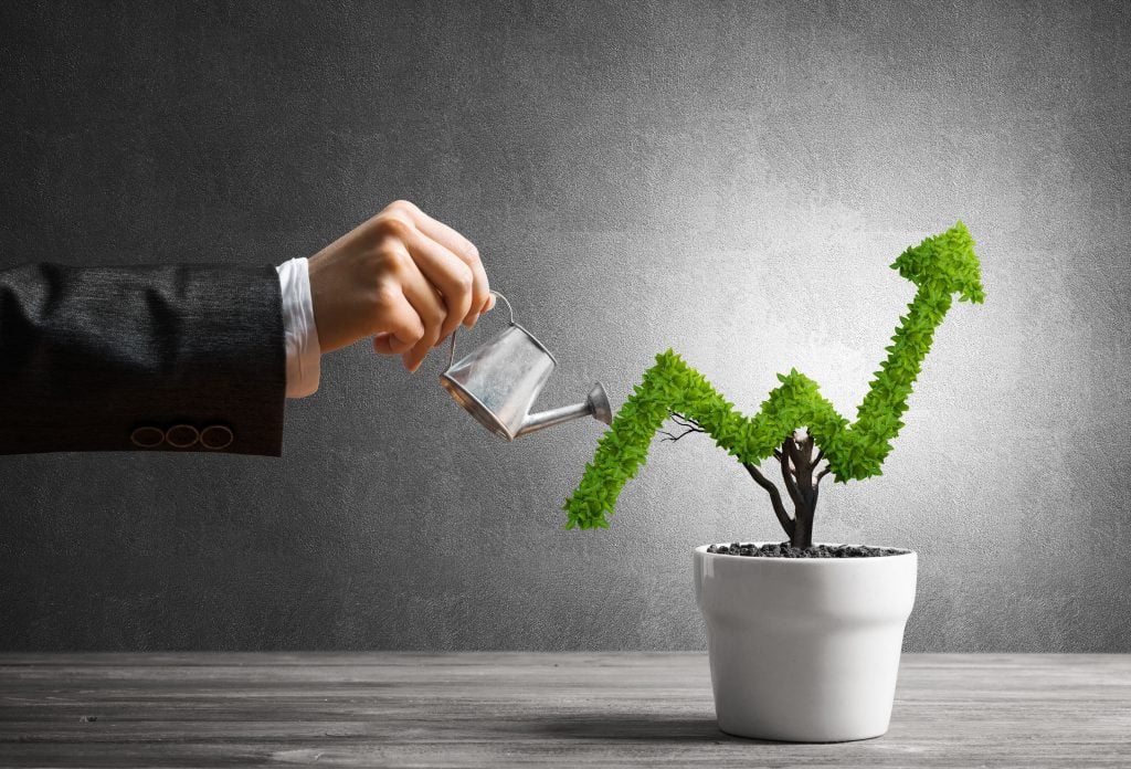 Woman's hand watering a plant in the shape of a growing stock chart.