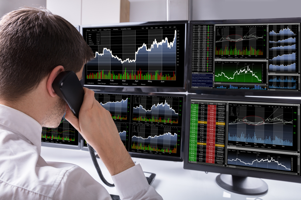 Stock broker on phone in front of multiple monitors with data