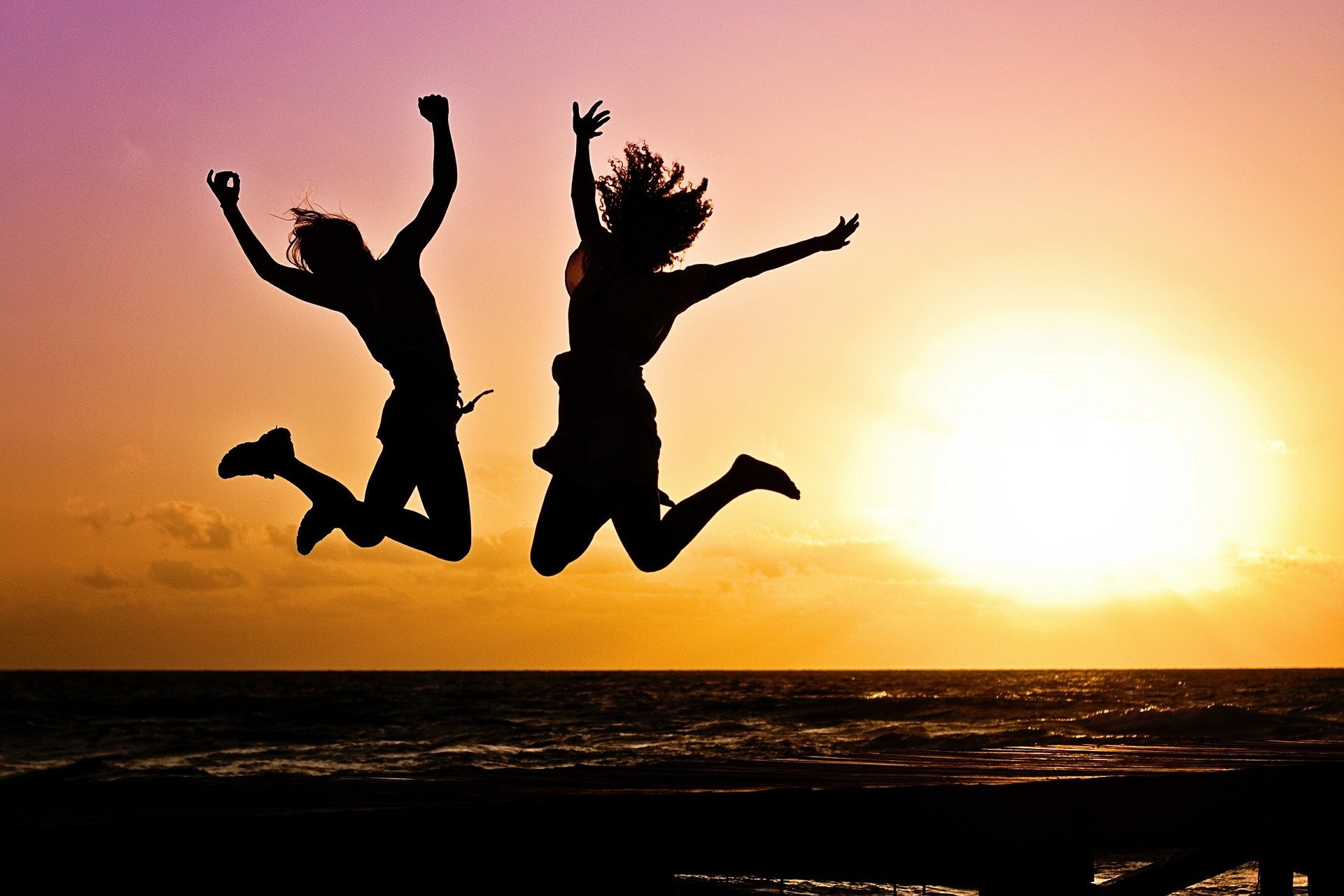 Two people jump with a setting sun in the background.
