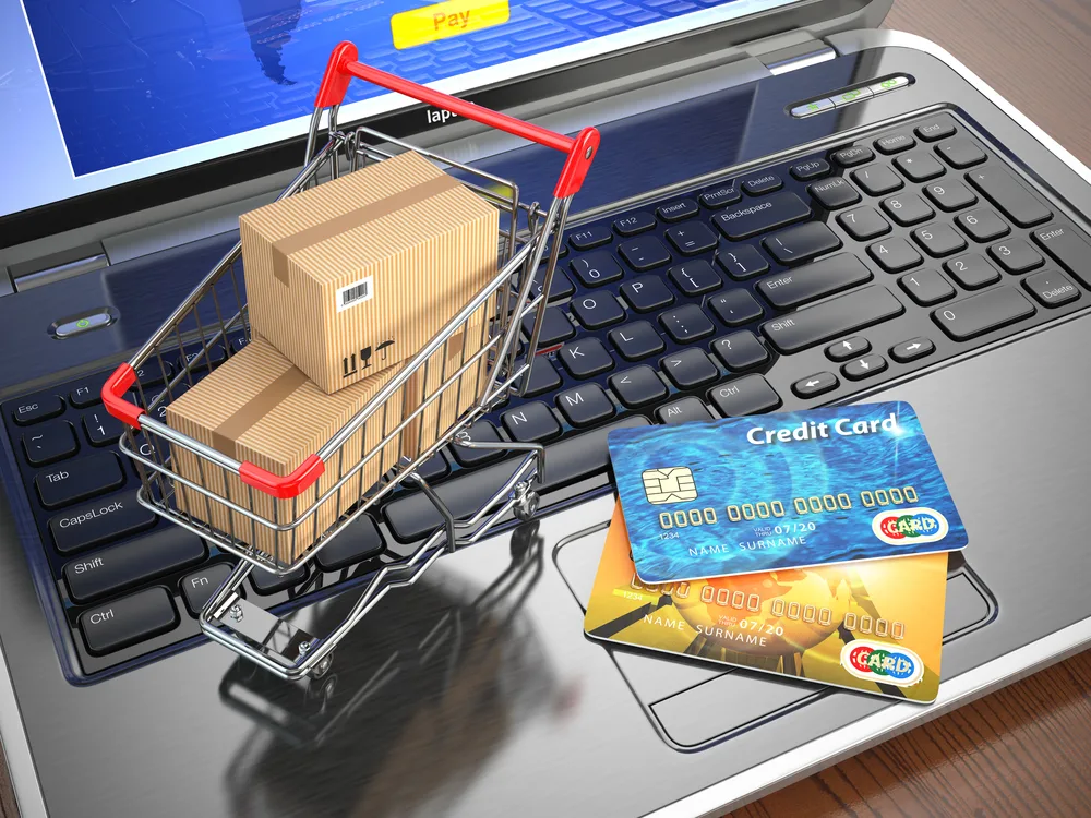 an image of a laptop holding a shopping cart filled with boxes and two credit cards