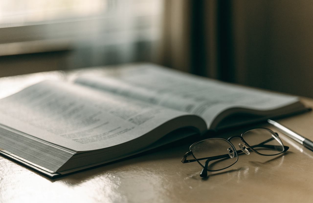 A bound quarterly financial report open on a desk beside reading glasses and a pen, soft window light from the left
