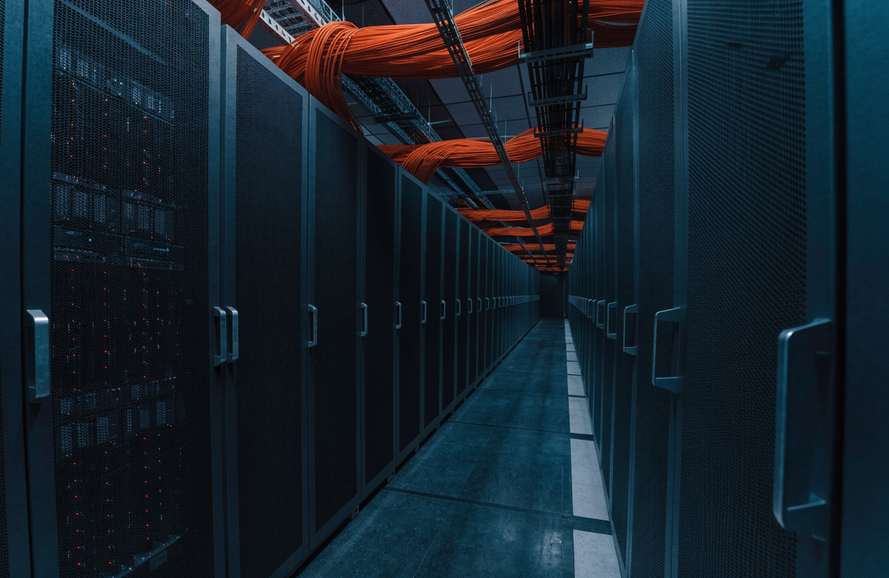A data center aisle with dense bundles of orange fiber cabling running overhead between server racks